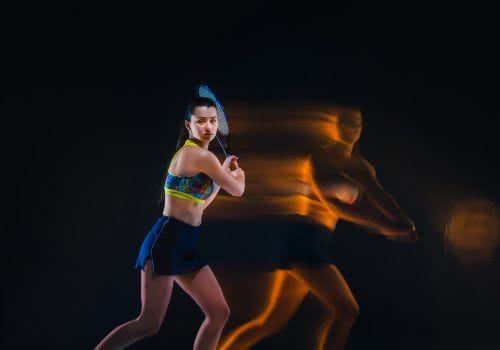 Portrait of beautiful girl tennis player with a racket on dark studio background. Stroboscope shooting technique