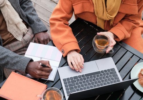 Close-up of business people sitting at the table drinking tea and working on laptop